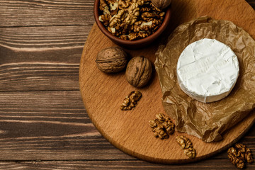 Camembert or Brie cheese with walnut kernels on wooden wooden background. Copy space. white mold grows on top Penicillium camemberti. 