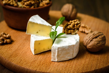Camembert or Brie cheese with walnut kernels on wooden wooden background. Copy space. white mold grows on top Penicillium camemberti. 