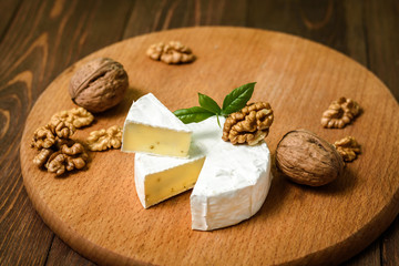 Camembert or Brie cheese with walnut kernels on wooden wooden background. Copy space. white mold grows on top Penicillium camemberti. 