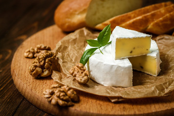 Camembert or Brie cheese with walnut kernels on wooden wooden background. Copy space. white mold grows on top Penicillium camemberti. 