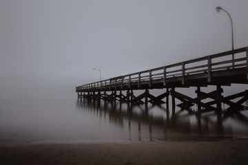 Fishing pier disappearing into the sea in foggy conditions. Dramatic seascape, creepy moody scene. 
