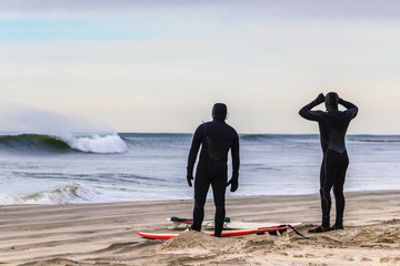 Surfers preparing to enter the ocean in wetsuits to catch large waves. Winter surfing - Atlantic Ocean
