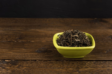 dry green tea in a clay bowl isolated on wooden table on black background