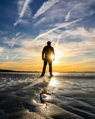 Silhouette of a man on the beach, with setting sun burst seen through the figure. Vacation / holiday outdoor adventure scene. 