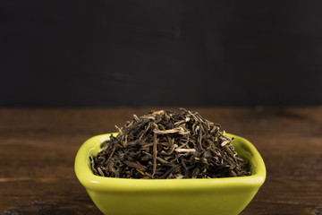 dry green tea in a clay bowl isolated on wooden table on black background