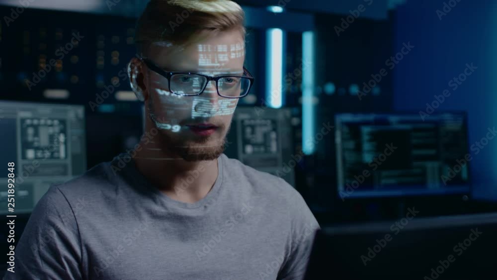 Poster Portrait of Software Developer / Hacker Working on Computer, Projected Code Numbers and Characters Reflect on His Face. Dark Room Full of Electronics, Computers, Displays. Hacking or Programming