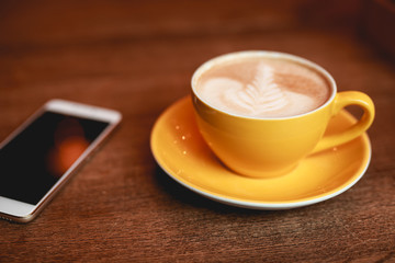 Fototapeta na wymiar Coffee-break, latte in a yellow cup and smartphone on a desk
