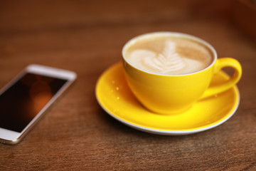 Fototapeta na wymiar Coffee-break, latte in a yellow cup and smartphone on a desk