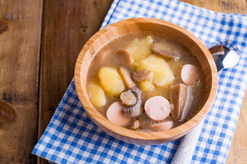 soup with sausages and potatoes on a wooden background in a bowl. Traditional German rustic soup. Rustic style photo. Free space for text.