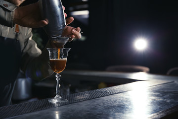 Barman pouring martini espresso cocktail into glass at counter, closeup. Space for text
