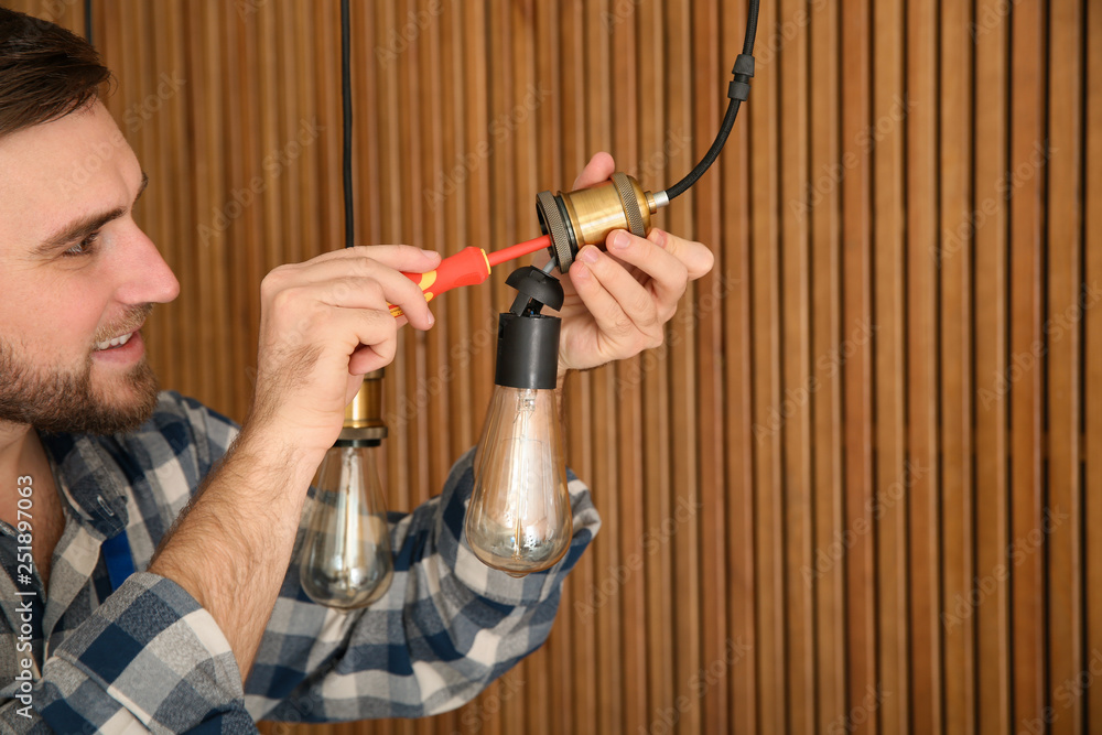 Wall mural Electrician with screwdriver repairing ceiling lamp against wooden background. Space for text