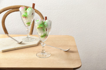 Glasses with snow ice cream dessert on table against light wall. Space for text