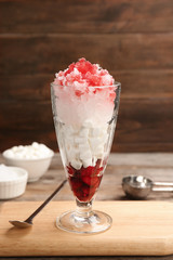 Glass of snow ice cream with raspberry and  marshmallow on table against wooden background