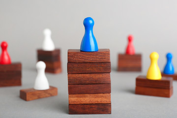 Board game piece on wooden blocks dominating other figures against grey background. Victory concept