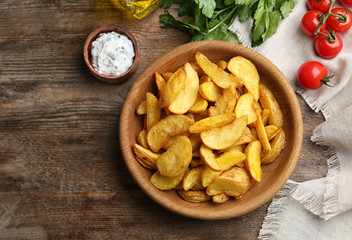 Bowl with tasty baked potato wedges on wooden background, top view. Space for text