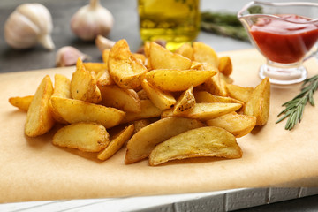 Delicious baked potato wedges and sauce on wooden board, closeup
