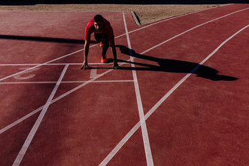 young muscular athlete is at the start of the race tracks line at the stadium. Sports concept