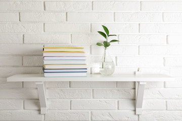 Shelf with stack of hardcover books hanging on brick wall