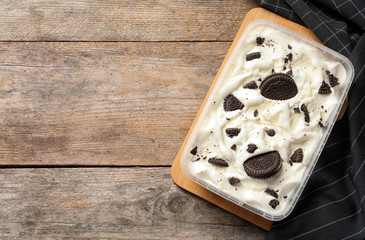 Container of ice cream with chocolate sandwich cookies on wooden background, top view. Space for text