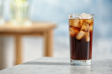 Glass of cold cola on table against blurred background. Space for text