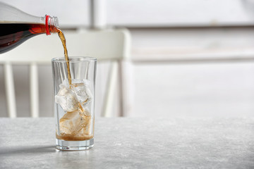 Pouring cola from bottle into glass on table. Space for text