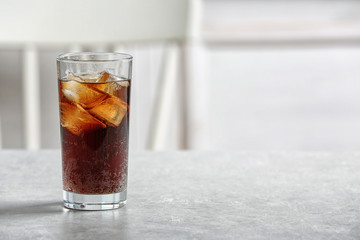Glass of cold cola on table against blurred background. Space for text