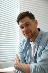 Fototapeta premium Handsome man near window with Venetian blinds