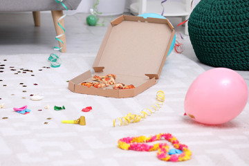 Pizza box with leftovers on messy apartment floor. After party chaos