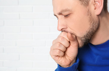 Man suffering from cough near brick wall. Space for text