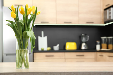 Glass vase with tulips on table in kitchen
