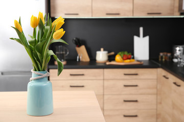 Ceramic vase with tulips on table in kitchen