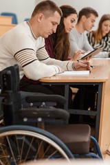 Side view of concentrated student sitting at table and reading material during lecture. Disable man...