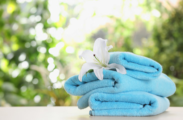 Obraz na płótnie Canvas Stack of clean soft towels and flower on table against blurred background. Space for text