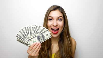 Portrait of a cheerful pretty girl looking at camera with bunch of money banknotes isolated over...