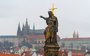 Prague, Czech Republic. Statue of St. John the Baptist on famous historical Charles Bridge with Prague Castle in background.