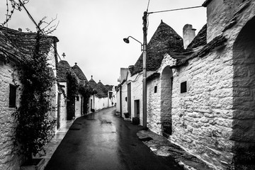 Black and white view of Alberobello street with typical buildings named Trulli in a rainy day, Puglia, Italy