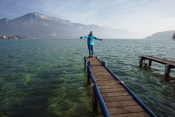 A happy tourist girl standing in the morning on a jetty at Lake Annecy with a mountain in the background France