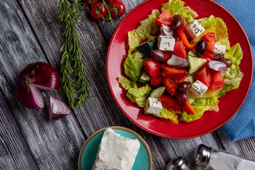 Greek salad of fresh cucumber, tomato, sweet pepper, lettuce, red onion, feta cheese and olives with olive oil on wooden background. Healthy food