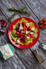 Greek salad of fresh cucumber, tomato, sweet pepper, lettuce, red onion, feta cheese and olives with olive oil on wooden background. Healthy food