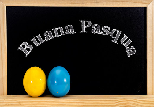 Easter frame with painted eggs and chalkboard. Happy Easter in white chalk. Happy Easter in italian : buana pasqua