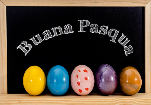 Easter frame with painted eggs and chalkboard. Happy Easter in white chalk. Happy Easter in italian : buana pasqua