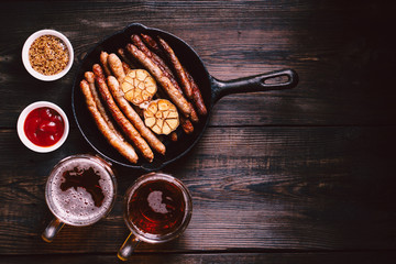 beer and snacks. bar table. restaurant, pub, oktoberfest food. two mugs of craft lager and frying pan with delicious homemade grilled sausages. friday party atmosphere, craft brewery concept