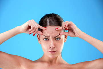 Signs of aging. Portrait of shocked young woman is looking at camera with disappointedly while touching her wrinkles on forehead on blue background