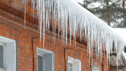 Ice stalactite hanging from the roof with red brick wall. Icicles are very dangerous for people's life. Poor thermal insulation of the roof leads to the formation of icicles.Natural seasonal phenomena