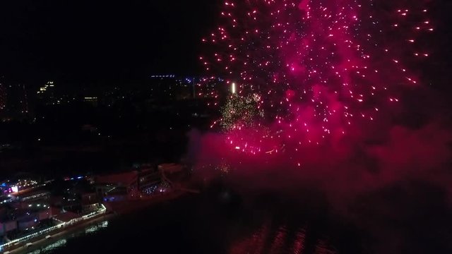 Different colors of firecracker moving up, burning and bursting in the evening sky, bird's-eye view. Amazing scene of fireworks above the urban illumination shine city at celebration, aerial view.