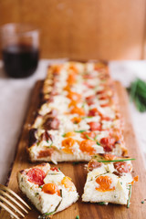 Homemade pie ( quiche) with ricotta, fresh colored tomatoes ,rectangular shapes on a cutboard,cut in cube with a wine glass,  frontal view, wooden rustic background