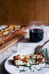 Homemade pie ( quiche) , with ricotta, and fresh colored tomatoes ,cut in slice in a dish with golden fork, glass of wine,rectangular shapes, frontal view ,rustic setup, natural ligt.