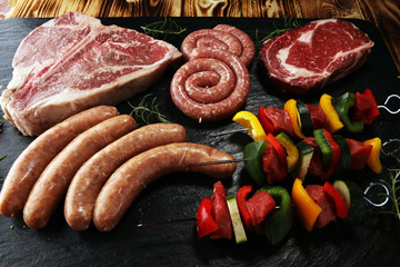 Assorted delicious raw meat with vegetable on a barbecue with t-bone steak, sausages and meat...