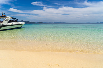 Speed boat for tourists anchored on the beach on the island with clear sea water, clean yellow sand, mountains in distance and beautiful sky.