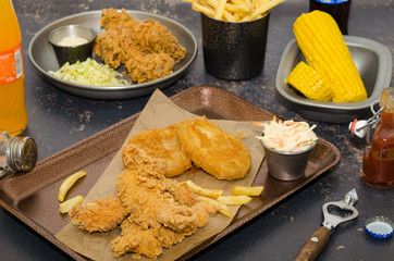 Dinner table with fried chicken wings and strips, roasted potatoes, french fries, coleslaw and sauces. Homemade southern fried chicken. Fried chicken meal